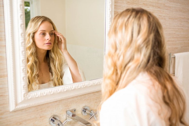 Девушка смотрит в зеркало в ванной